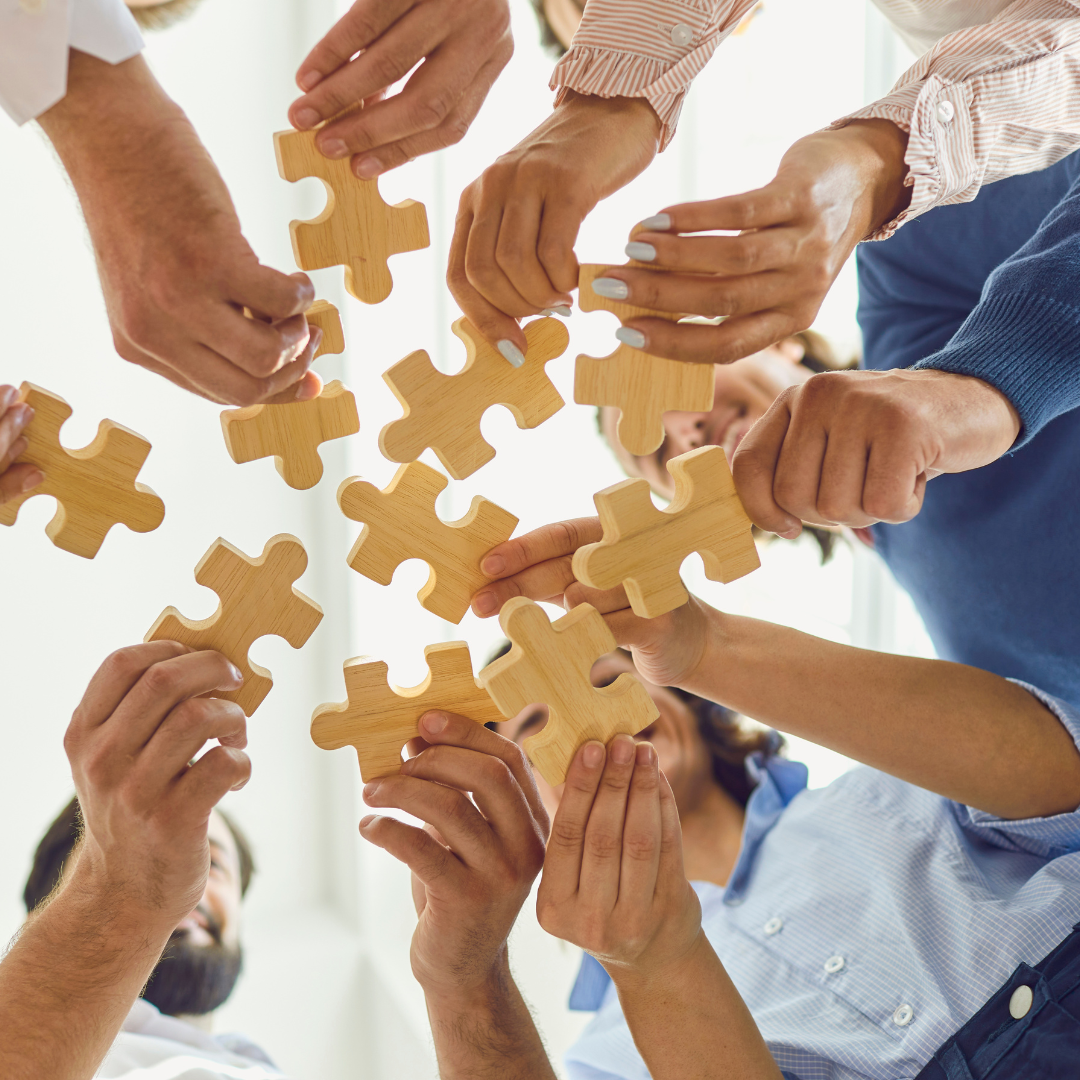 Wings Technical Services-recruitment company in qatar Multiple hands holding wooden puzzle pieces, reaching towards the center to fit them together, symbolizing teamwork and cooperation.