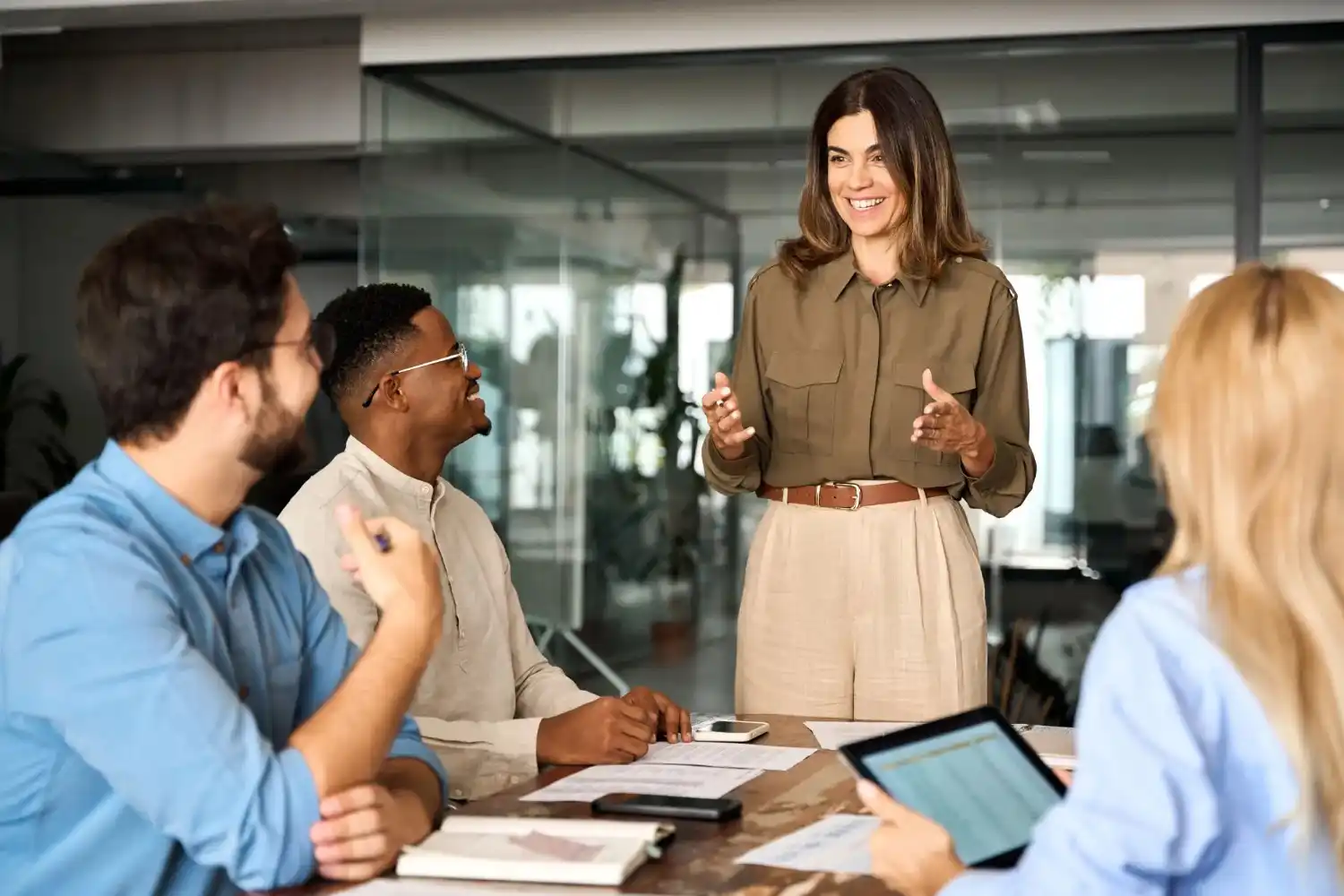 Four people having a meeting in a modern office, with one person standing and speaking while the others sit and listen.