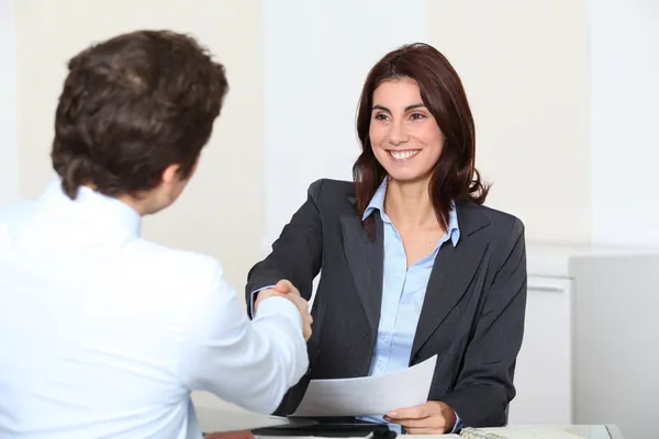 A woman in suit and a man shake hands in a professional office setting, symbolizing collaboration and agreement.